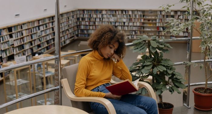 tan-skinned young Black woman or teen reading in a library