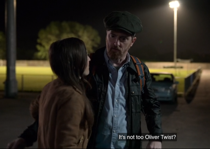 a still of Beard wearing a flat cap and looking at Jane as he says, "It's not too Oliver Twist?"