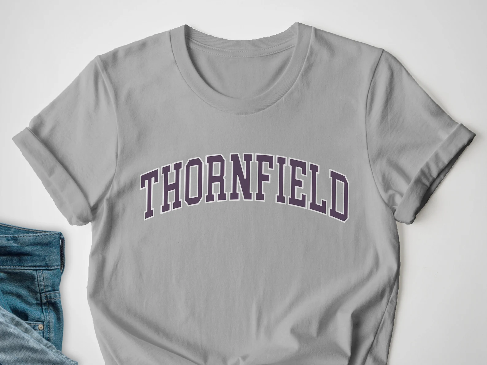 a grey t-shirt with purple all-caps text reading "Thornfield" in a font that looks like the shirt for a college