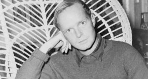 black and white image of Truman Capote seated in a wicker chair with his head resting on his hand