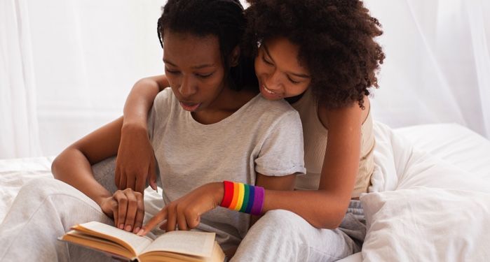 two Black women reading a book on a bed