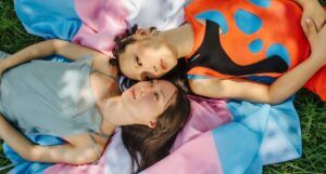 Image of two queer people of color lying on a trans flag
