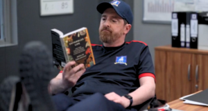 a still of Coach Beard reading Entangled Life at his desk