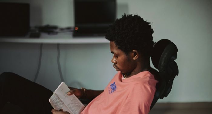 Black man with kinky hair leaning back in a chair reading a book