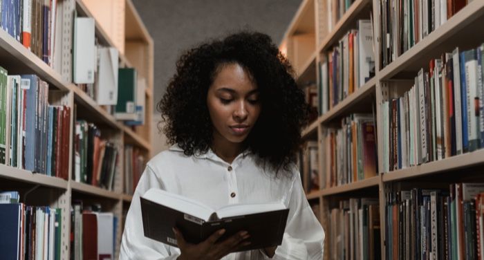 Black woman reading with a white blouse in a library