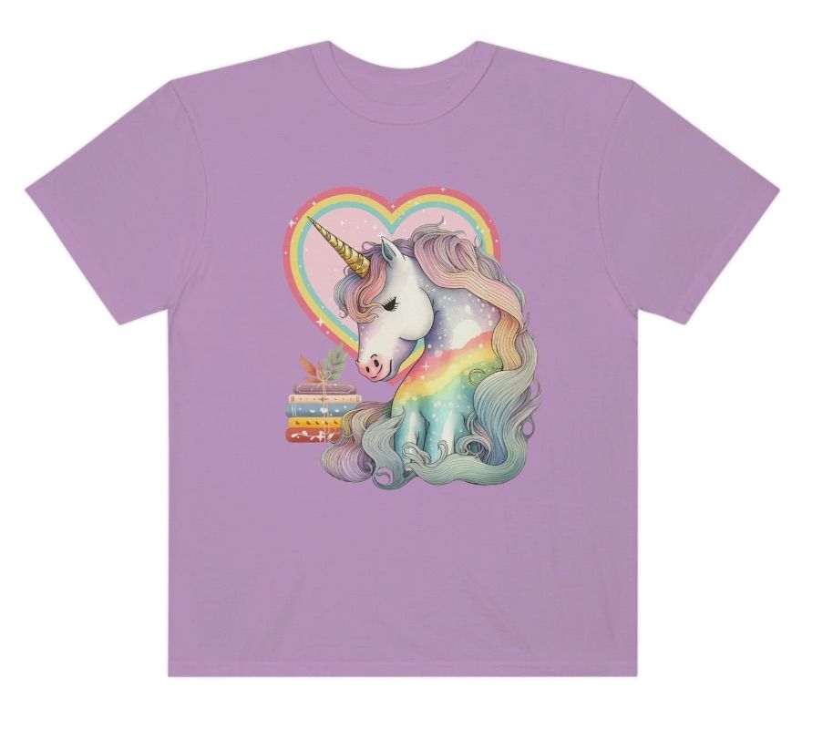 Image of a rainbow unicorn with a stack of colorful books on a purple shirt 