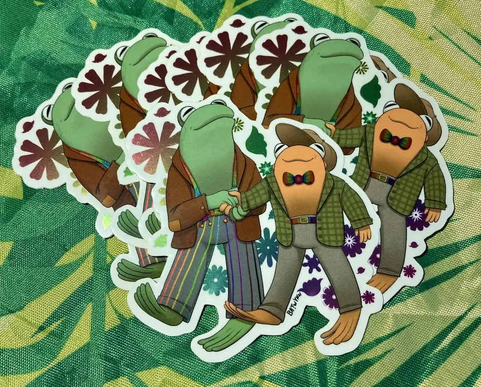 Image of a Frog and Toad sticker. They are a merry couple with pride bowties and pants. 