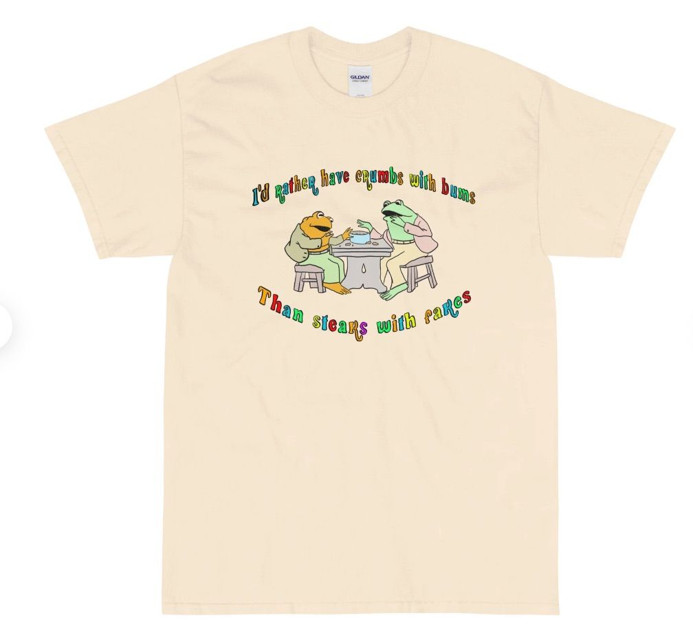 Image of a t-shirt with Frog and Toad on it. In rainbow text are the words "i'd rather have crumbs with bums than steaks with fakes."