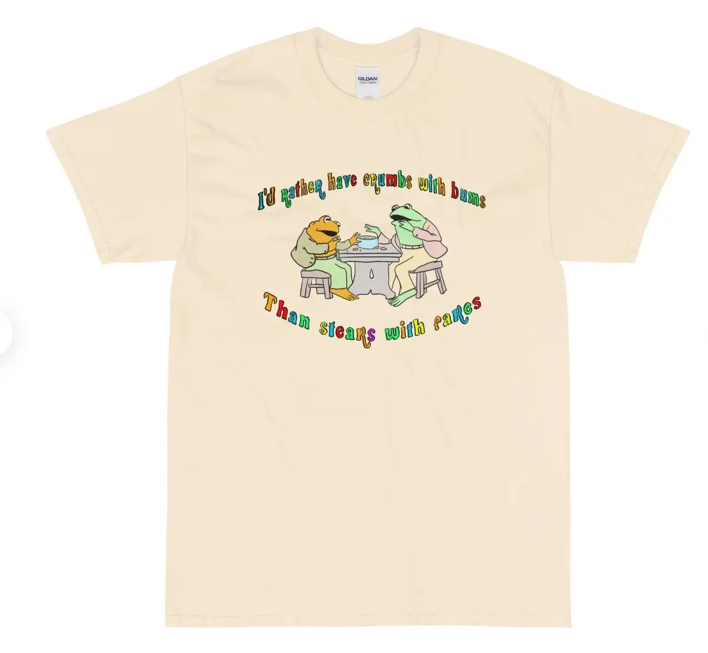 Image of a t-shirt with Frog and Toad on it. In rainbow text are the words "i'd rather have crumbs with bums than steaks with fakes."
