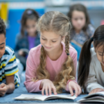 a photo of three kids on the floor reading. They are smiling