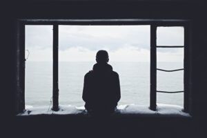 person alone sitting and looking out of a big window