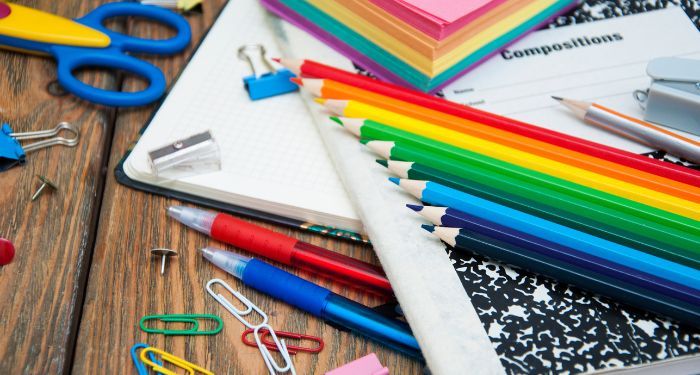assortment of colored pencils, notebooks, multicolored paper clips, and other school supplies on a wood surface