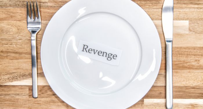 a white plate with a silver fork and knife setting around it. The dish contains a piece of paper with the word "revenge" printed in black text