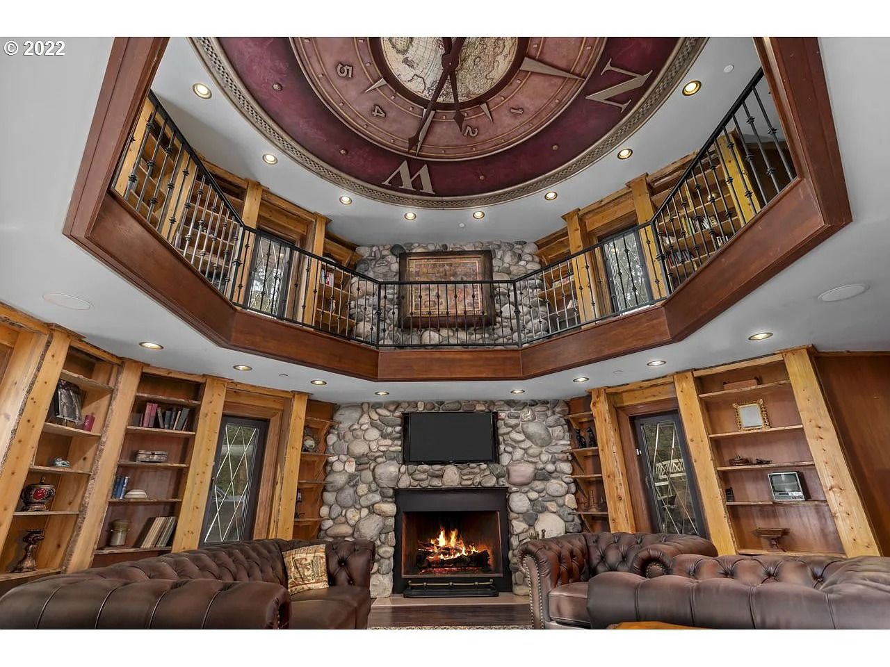 a photo of a two-story library with built in shelves and a large globe set into the ceiling with clock hands