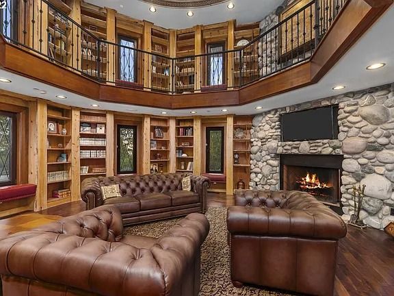 a photo of a two-story library with built in shelves, leather couches, a fireplace, and a wall-mounted TV