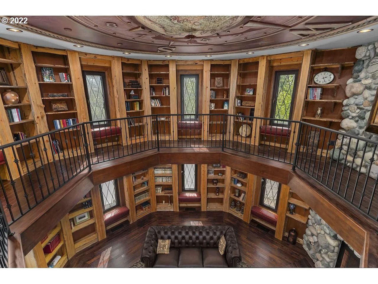 a photo of a two-story library with built in shelves and a large globe set into the ceiling and a leather couch on the ground floor