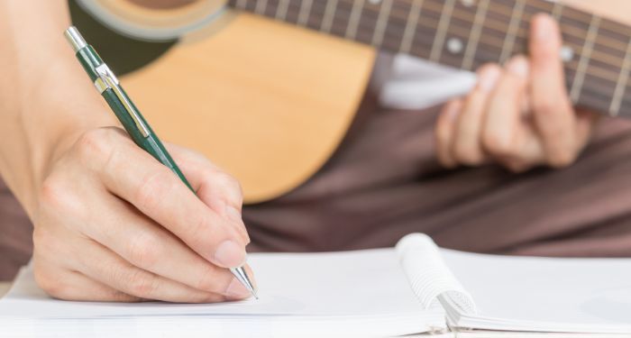 hands writing in a notebook while playing an acoustic guitar