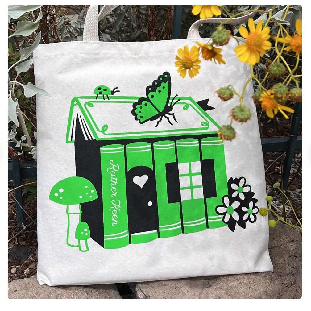 Image of a tote with a green cottage made of books. 