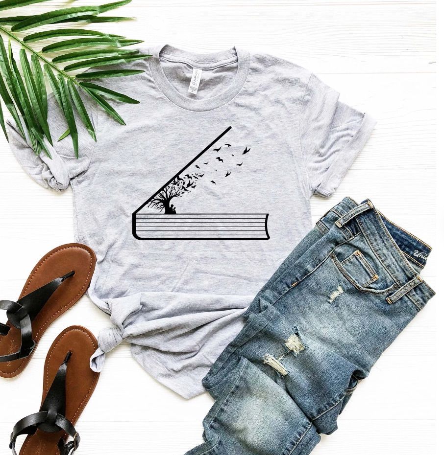 Image of a gray t-shirt featuring an open book, tree, and birds flying away. 
