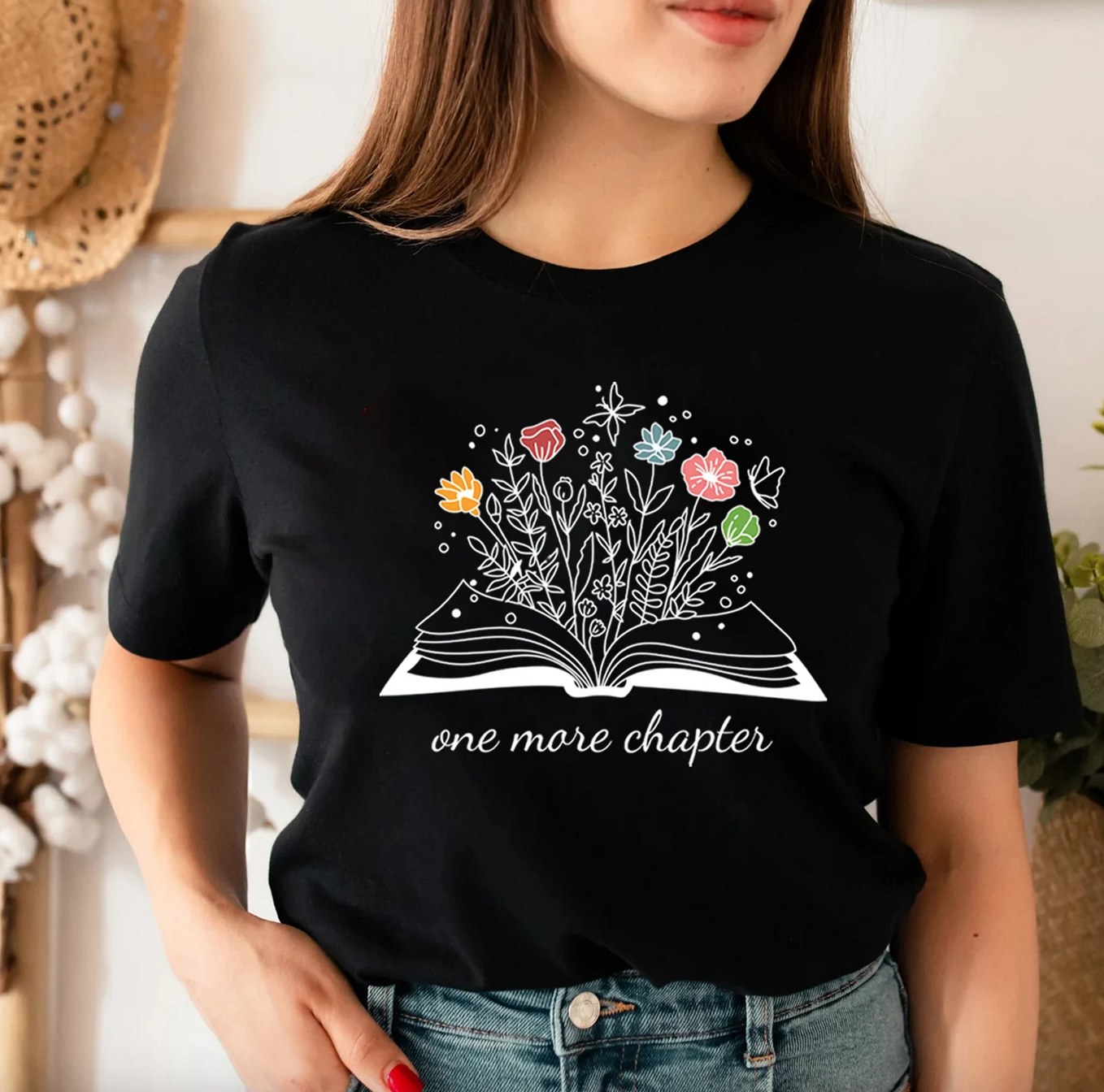 Black T-shirt with a print of an open book with flowers growing out of it and the text "one more chapter"