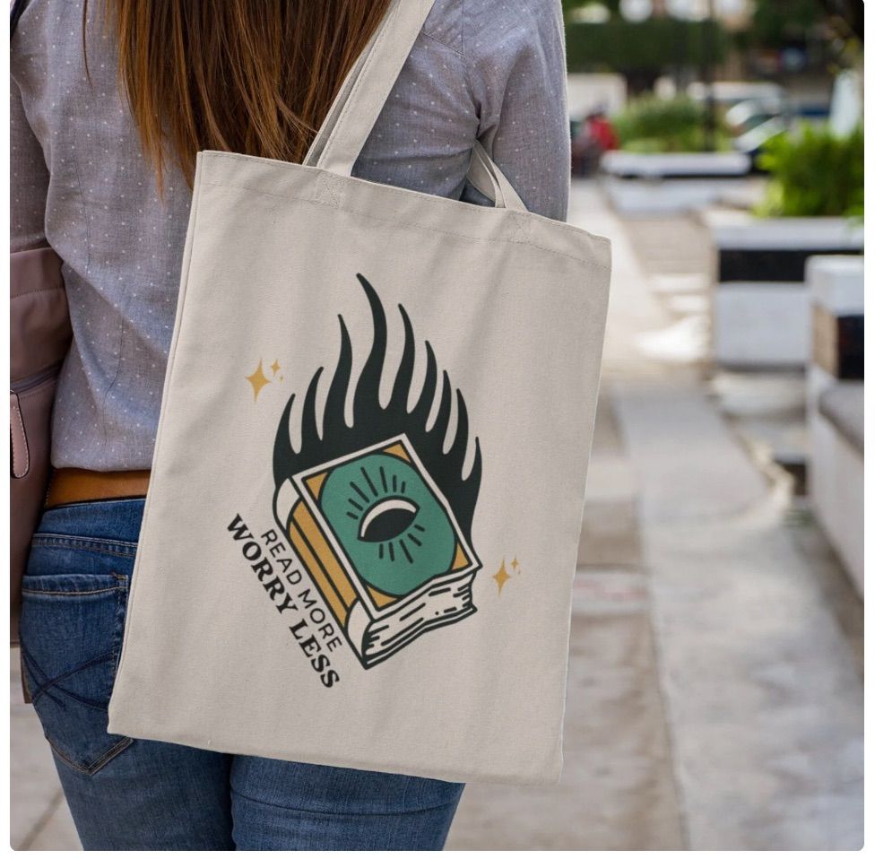 Image of a canvas tote bag with a book on it. Beside the book says "read more, worry less."