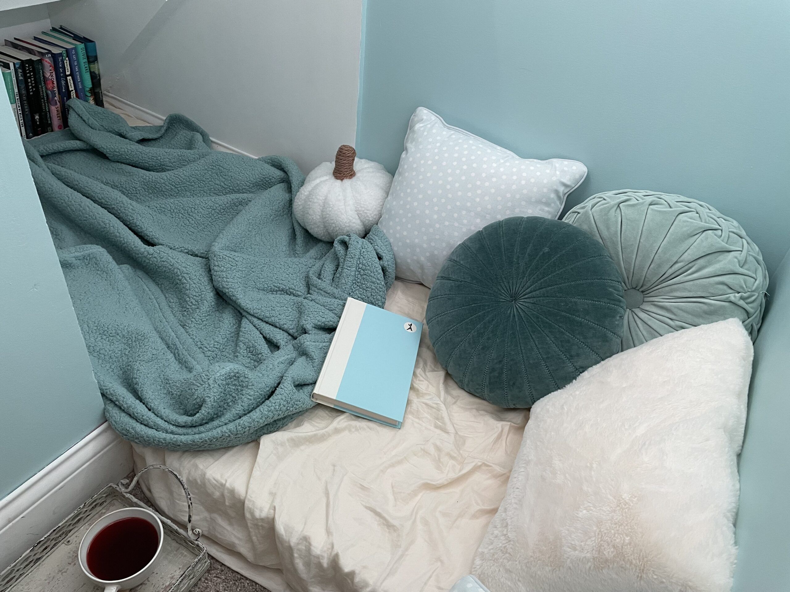 reading nook underneath with stairs with blue and white pillows, a blue blanket, a cup of tea, and books