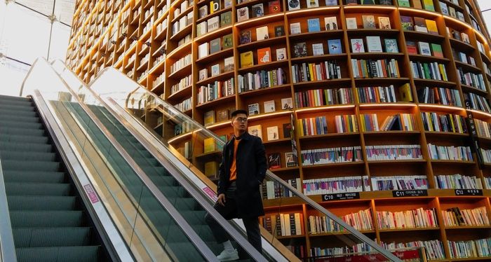 bookstore with huge shelf, with Asian man riding escalator