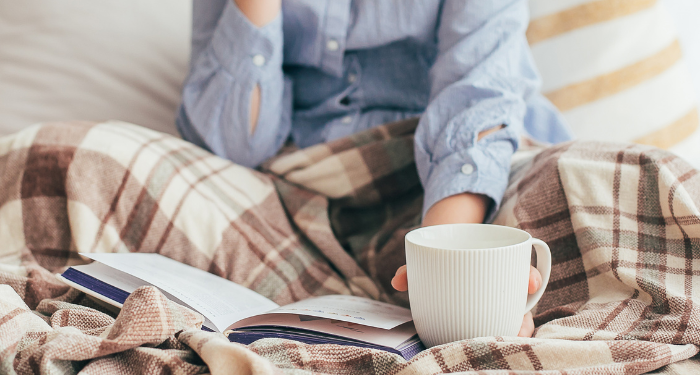 a photo of someone reading in bed, holding a mug