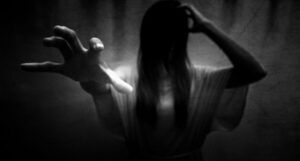 black and white image of a ghostly woman in a white dress with one hand outstretched and her dark hair obscuring her face