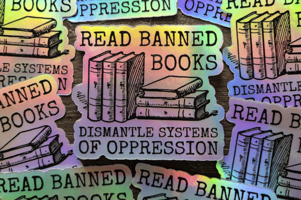 holographic sticker with stacks of books and book spines and the text "Read banned books dismantle systems of oppression"