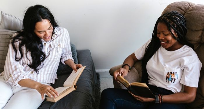one tan-skinned woman with long, black hair reading next to a brown-skinned Black woman with box braids who is also reading