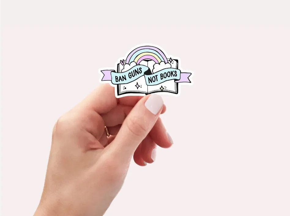 Image of a white hand holding a sticker that reads "ban guns, not books."