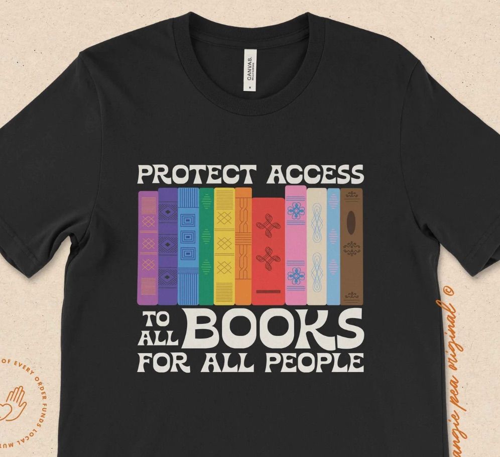 Image of a black shirt with white text reading "protect access to all books for all people." It has colorful book spines on it. 