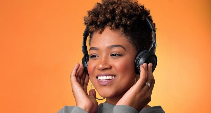 brown-skinned Black woman with headphones one; orange background