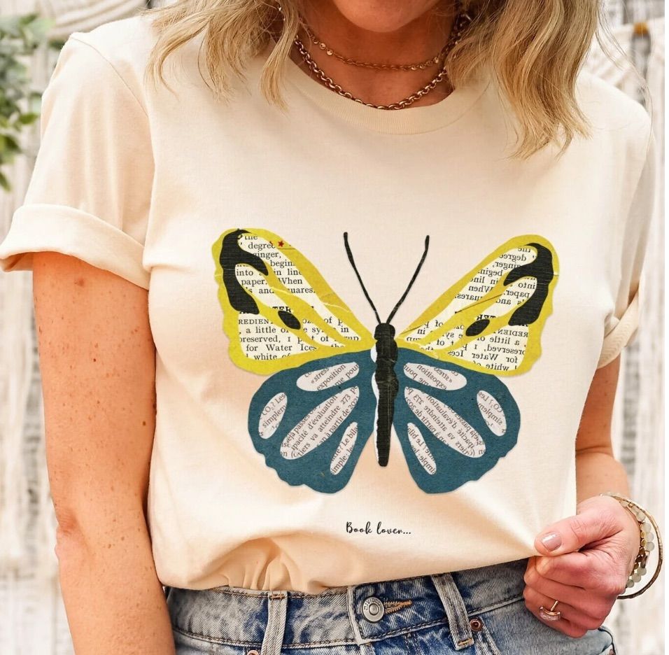 Image of a person wearing a cream t-shirt. The shirt has a butterfly in yellow and blue and its wings are made of book pages. 