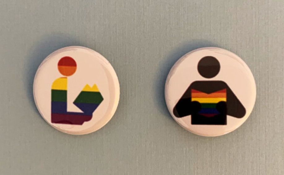 Pair of buttons featuring the library symbol, with the book colored in like a rainbow. 