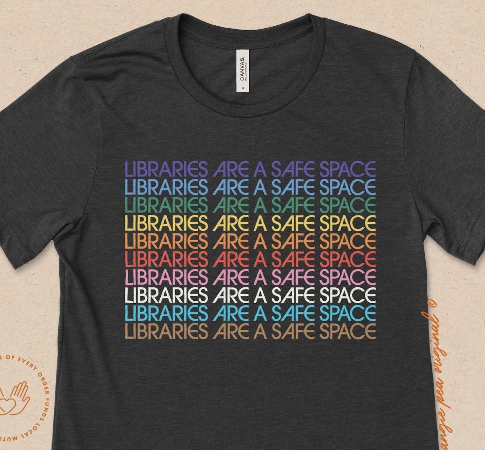 Image of a black t-shirt with the sentence "libraries are a safe space" in a rainbow of colors. 