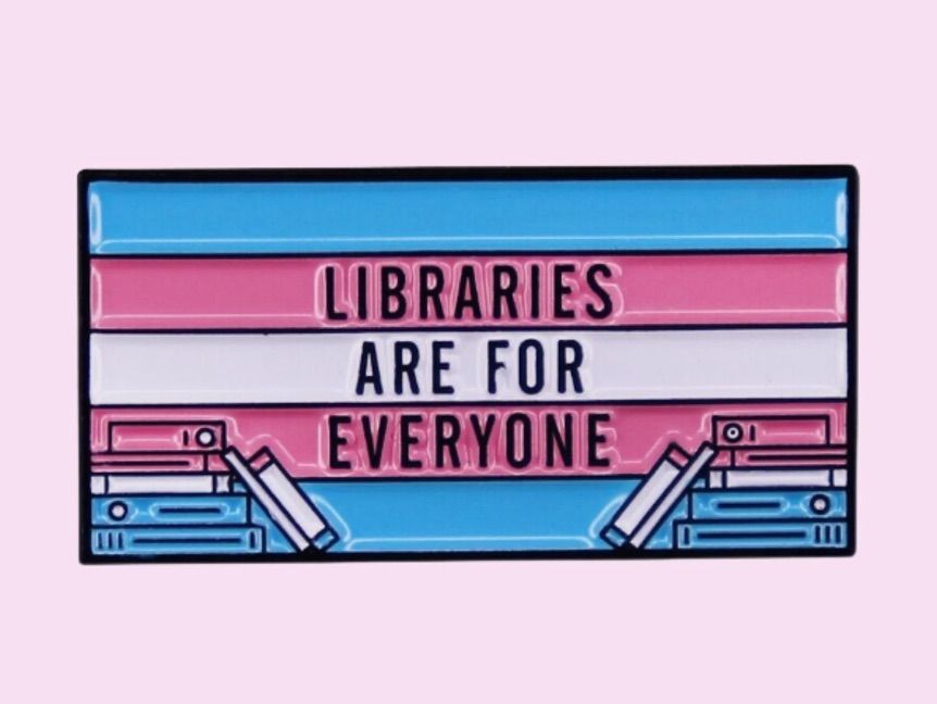Image of a trans flag enamel pin with the phrase "libraries are for everyone." 
