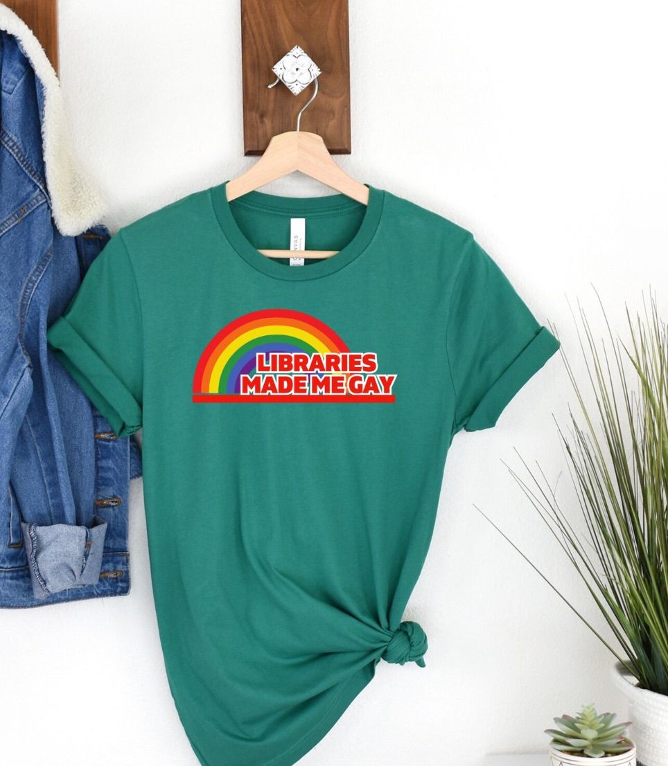 Image of a green t-shirt with a logo similar to the reading rainbow logo. It says "Libraries made me gay."