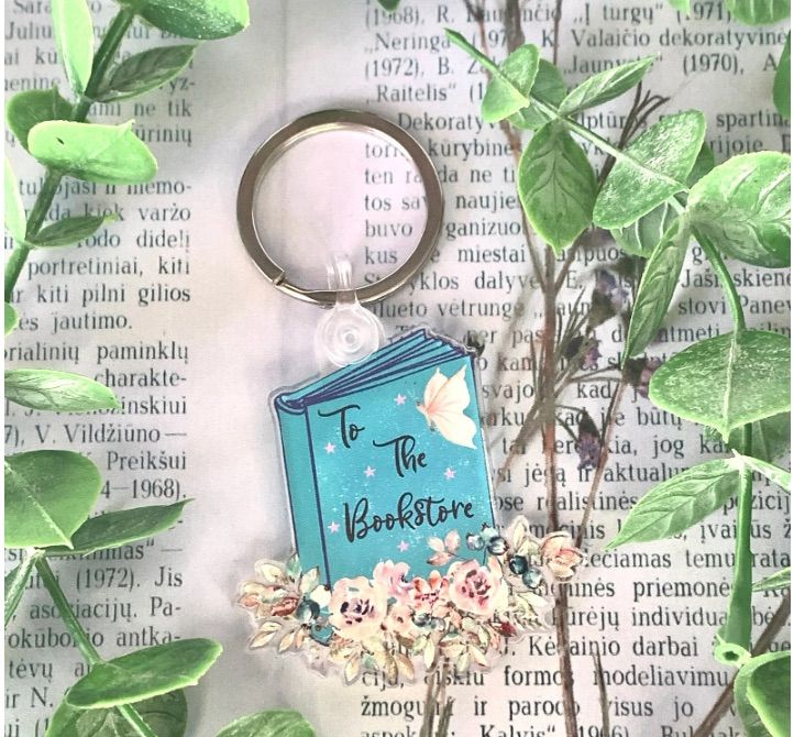 Image of a book keychain that says "to the bookstore." The book on the keychain has a pink butterfly. 