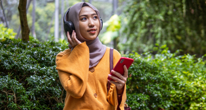 a photo of a person wearing a hijab listening to headphones at a park