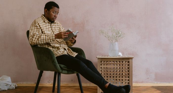 brown-skinned Black man reading against a light pink background
