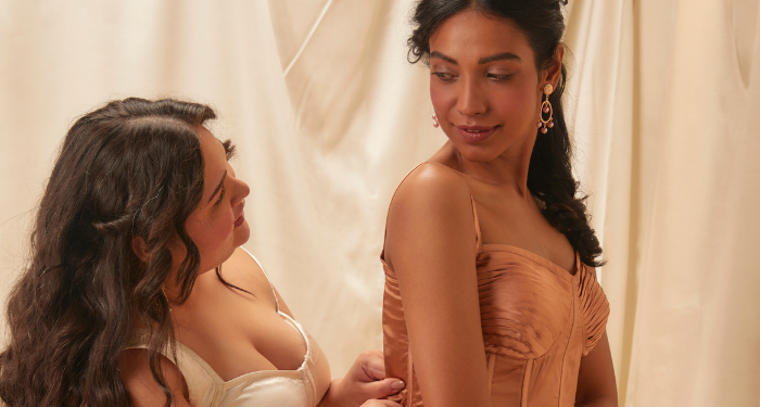 a photo of two women in Regency-style outfits, one dressing the other. They are looking at each other intently