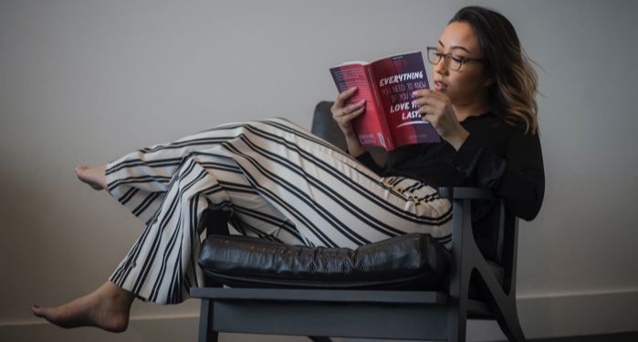 lightly tanned-skinned woman reading a book in a chair with her feet up