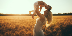 a photo of a mom smiling and lifting her son up outside at sunset