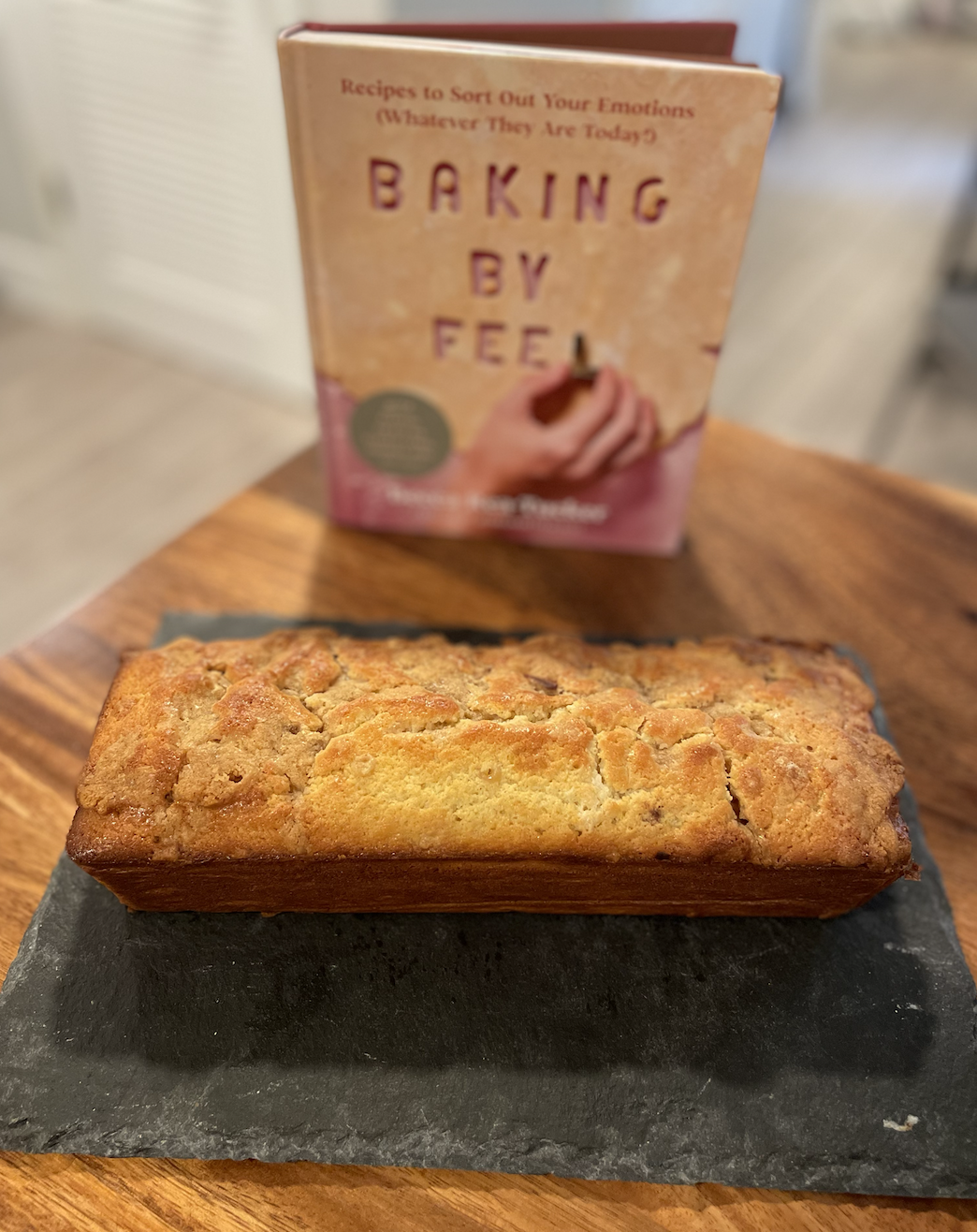photo of a poundcake loaf with a crumbled topping on a slate serving board on a wooden table with the cookbook Baking by Feel