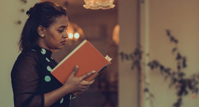 brown-skinned Black woman with polka dot dress is reading an orange book