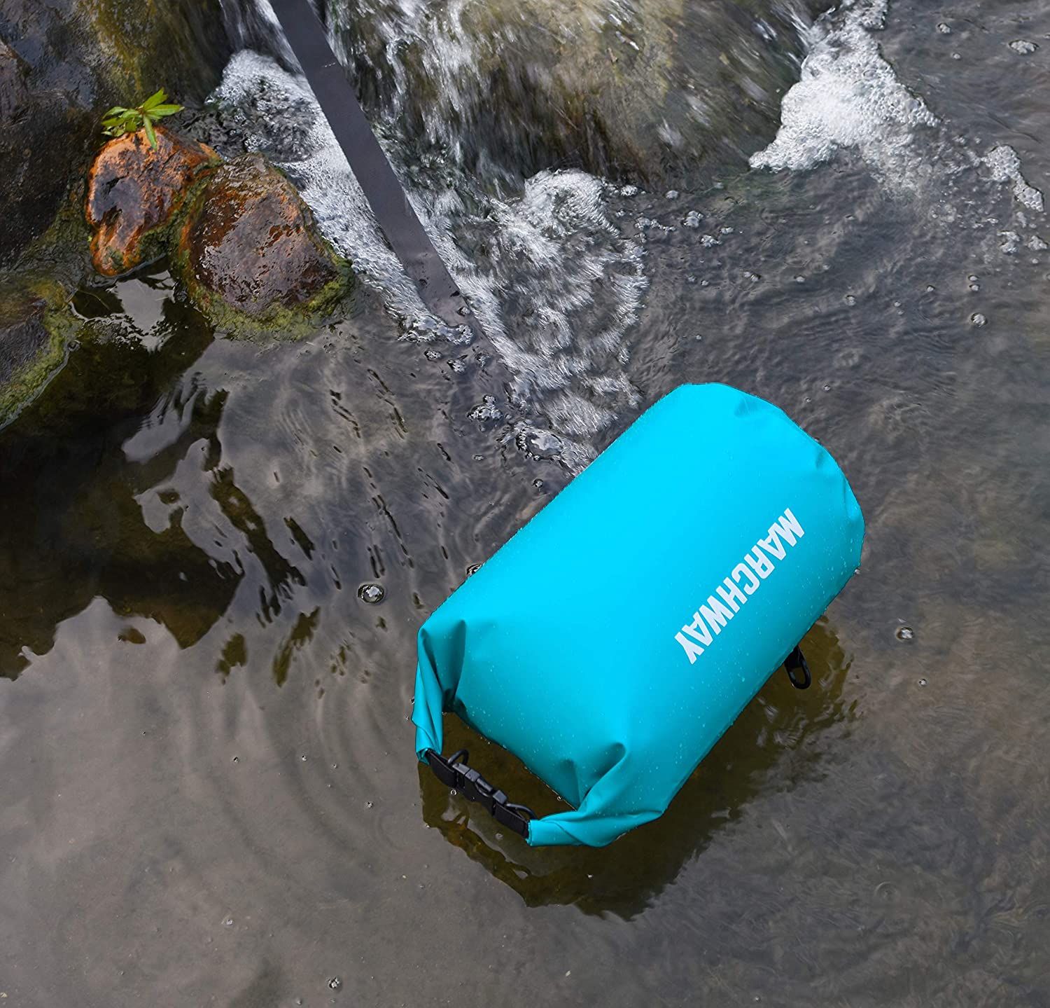 A teal dry bag closed and floating on a stream