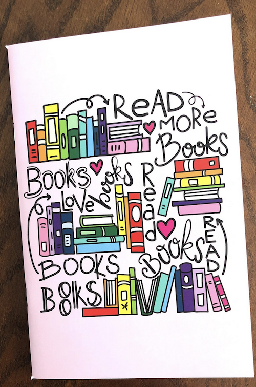 thin notebook with graphic colorful illustration that says read more books with stacks of books