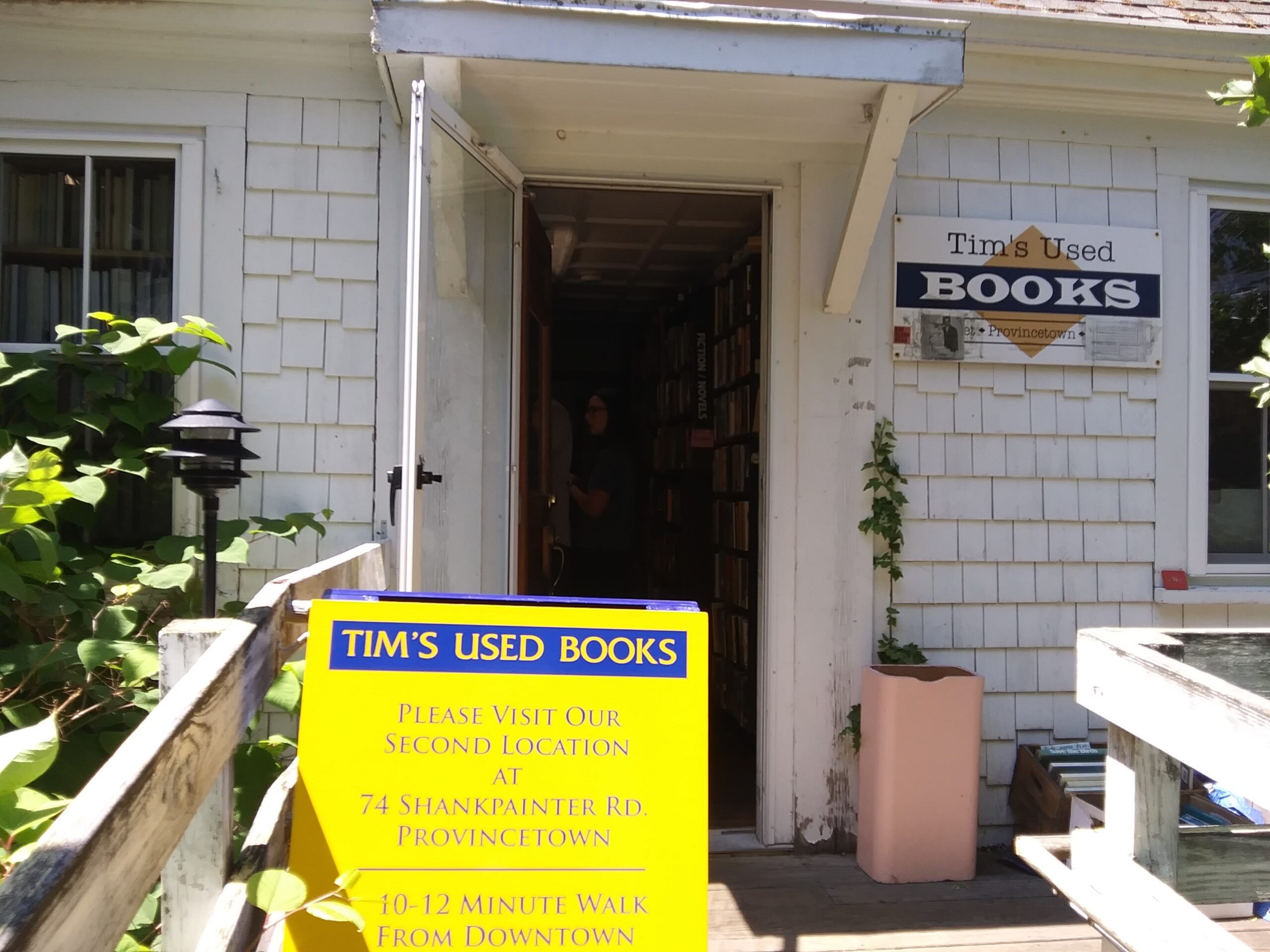 A close-up of the front door of a white shingled house. To the right of the door is a sign that says Tim's Used Books